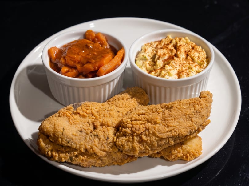 Fried fish fillets with two side dishes, one with carrots and the other with a creamy dip.